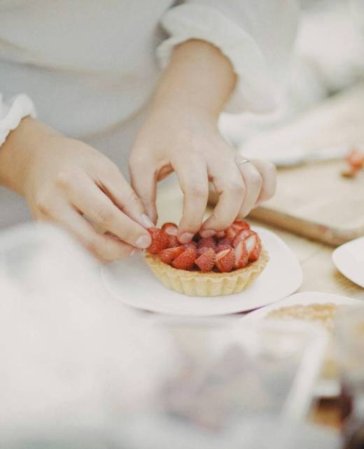 person holding sliced strawberries on white ceramic plate